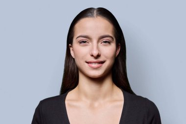 Gri stüdyo arka planında gülümseyen güzel bir genç kadının portresi. Kameraya bakan uzun siyah saçlı 18 yaşında başarılı bir kadın. Güzellik yaşam tarzı sağlık gençlik kavramı