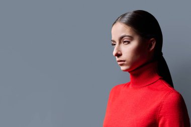 Gri arka planda genç ciddi bir kadının portresi. Kırmızılı güzel, düşünceli kadın ileriye bakıyor. Reklam metni için mekanı kopyalıyor. Gençlik servisi moda eğitimi kavramı