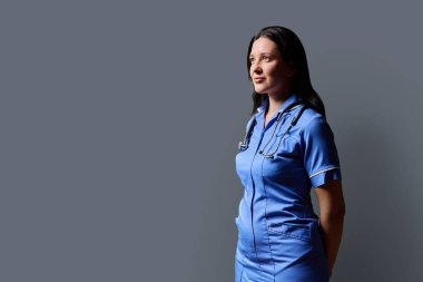 Gri stüdyo arka planında steteskop bulunan mavi üniformalı kadın doktor portresi, fotokopi odası. Tıp, insanlar, sağlık personeli, sağlık hizmetleri kavramı