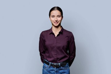 Gri stüdyo arka planında poz veren güzel, gülümseyen genç bir kadının portresi. Kameraya bakan 18 yaşında başarılı bir kız. Güzellik yaşam tarzı sağlık gençlik kavramı