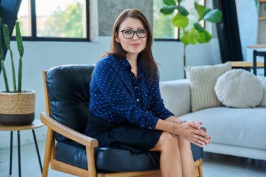 Sandalyede oturmuş kameraya bakarken gülümseyen orta yaşlı güzel bir kadının portresi. Yaşam tarzı, güzellik, sağlık, iş, iş, 40 'lar, kadınlar, insanlar kavramı