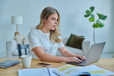 Masasında dizüstü bilgisayarlı ders kitaplarıyla oturan genç bir üniversite öğrencisi. Daktilo yazan defterler. Eğitim, eğitim, bilgi, gençlik kavramı