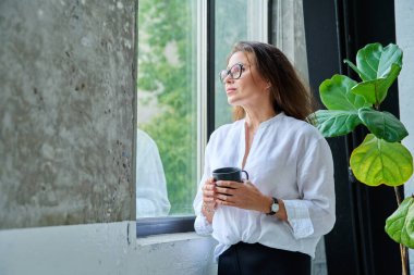 Ofisteki pencereye bakan orta yaşlı, ciddi bir kadın. Boş zaman, rahatlama, yaşam tarzı, iş molasında, iş adamları kavramı