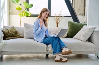 Genç ve güzel bir kadın internette sohbet konferansı için dizüstü bilgisayar kullanıyor. Evde, sandalyesinde oturuyor. İletişim öğrenmek için dijital teknolojiler boş zamanlarında sosyal medya bloglarında çalışır