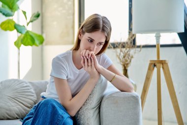 Üzgün, stresli genç bir kadın evinde, kanepede oturuyor. Duygular, sorunlar, ilişkilerde zorluklar, öğrenim, aile, zihinsel sağlık