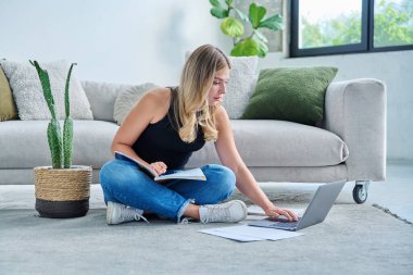 Evde dizüstü bilgisayarlı ders kitabı ile oturan genç bir kız öğrenci sınav için notlar alıyor. Eğitim e-öğrenim kursu internet dersleri gençlik yaşam tarzı