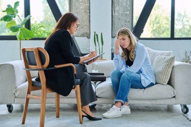 Üzgün olduğunu vurgulayan üzgün genç kadın terapi seansında kadın psikolog, ruh sağlığı danışmanı ve kanepede yan yana oturan sosyal psikolog ile ağlıyor.