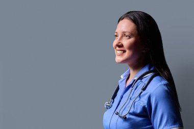 Orta yaşlı gülümseyen kadın doktor portresinin portresi. Mavi üniformalı, steteskoplu, gri stüdyo arka planı, fotokopi odası. Tıp, insanlar, sağlık personeli, sağlık hizmetleri kavramı