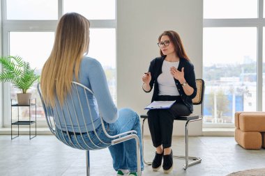 Orta yaşlı, kendine güvenen profesyonel kadın psikolog psikoterapist danışman ofiste birlikte oturan genç bir kadınla çalışıyor. Psikolojik hizmetler, bireysel terapi desteği