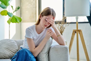 Üzgün, stresli genç bir kadın evinde, kanepede oturuyor. Duygular, sorunlar, ilişkilerde zorluklar, öğrenim, aile, zihinsel sağlık