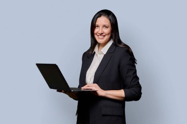 Dizüstü bilgisayarı açık arka planda başarılı orta yaşlı iş kadını portresi. Siyah takım elbiseli gülümseyen kadın kameraya bakıyor, bilgisayarı tutuyor. İş işi teknolojisi yönetim çalışanları