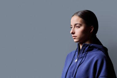 Gri arka planda genç ve ciddi bir genç kızın profil portresi. Güzel, çekici bir kadın ileriye bakıyor, reklam metni için fotokopi odası. Gençlik servisi moda eğitimi kavramı