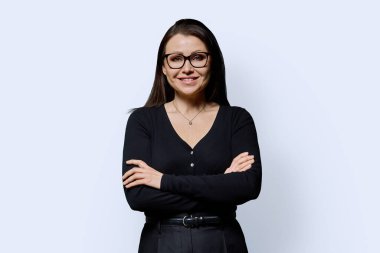 Beyaz arka planda çapraz kollu, kendine güvenen olgun bir kadının portresi. Gözlüklü, siyah elbiseli güzel bir kadın stüdyoda poz veriyor. Güzellik, sağlık, olgunluk, insan kavramı