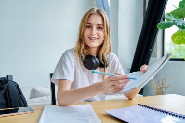 Webcam portresi, kulaklık takan üniversite öğrencisi, güzel sarışın kız evde oturuyor ve masada ders çalışıyor. Video konferansı sohbet çağrısı video çağrısı, uzaktan ders, online toplantı konsepti