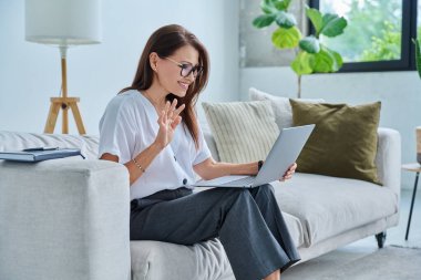 Orta yaşlı bir kadın uzaktan çalışıyor, video konferans görüşmeleri yapıyor, ofisteki koltukta dizüstü bilgisayar kullanıyor. Psikoloji oturumu çevrimiçi öğretim koçluğu vlog işi iletişimi