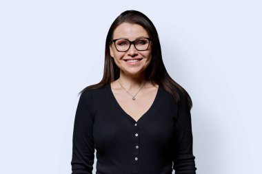 Beyaz arka planda gülümseyen olgun bir kadının portresi. Gözlüklü, siyah elbiseli güzel bir kadın stüdyoda poz veriyor. Güzellik, sağlık, olgunluk, insan kavramı