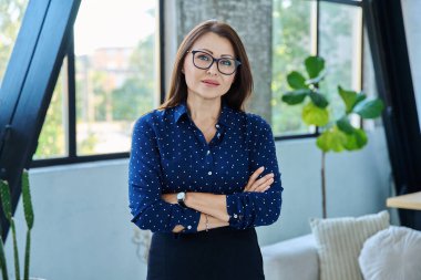 Kameraya bakan orta yaşlı, gülümseyen iş kadını portresi. Ofiste çapraz kollu 40 'lı yaşlarda kendinden emin bir kadın. İş yönetimi kariyeri olgun insanlar