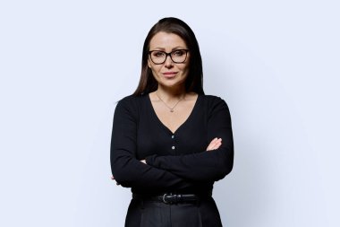 Beyaz arka planda çapraz kollu, kendine güvenen olgun bir kadının portresi. Gözlüklü, siyah elbiseli güzel bir kadın stüdyoda poz veriyor. Güzellik, sağlık, olgunluk, insan kavramı