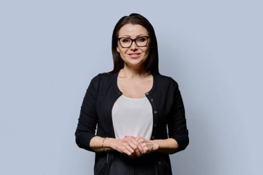 Gri arka planda gülümseyen olgun bir kadının portresi. Gözlüklü, siyah elbiseli güzel bir kadın stüdyoda poz veriyor. Güzellik, sağlık, olgunluk, insan kavramı