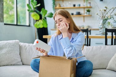 Genç, üzgün, karton kutuları internetten sipariş eden, cilt bakım ürünleri satın alan, ev yapımı kimyasallar alan, evinde kanepede oturan bir kadın. E-alışveriş, e-market, teslimat servisi.