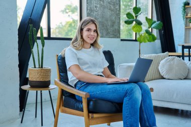 Kameraya bakan genç bir kadının portresi. Ev içinde dizüstü bilgisayarı olan bir sandalyede oturuyor. Üniversite öğrencisi sınava hazırlanıyor, bilgisayar başında yazı yazıyor, rahatlıyor, sosyal medyayı okuyor.