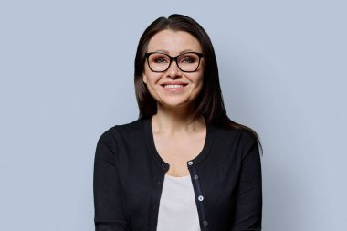 Gri arka planda gülümseyen olgun bir kadının portresi. Gözlüklü, siyah elbiseli güzel bir kadın stüdyoda poz veriyor. Güzellik, sağlık, olgunluk, insan kavramı