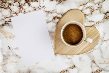 Mermer bir arka planda, içi boş kağıt parçasıyla kalp şeklinde bir tutacağa kahve.