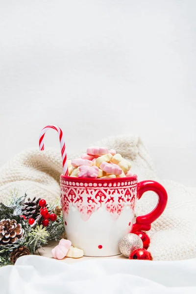 Red mug with marshmallows and winter ornaments on a white sheets