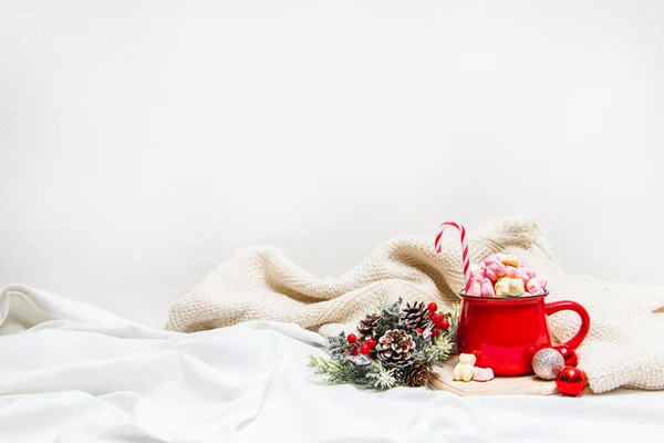 Red mug with marshmallows and winter ornaments on a white sheets
