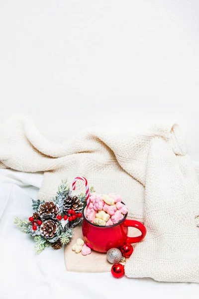 Red mug with marshmallows and winter ornaments on a white sheets