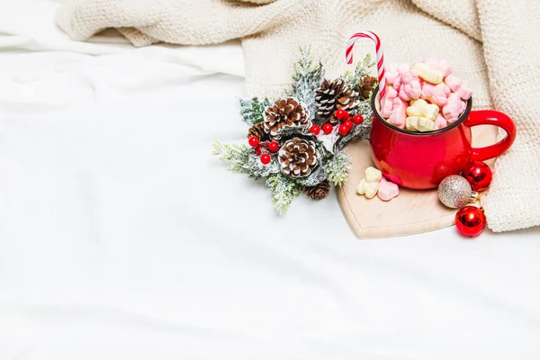 Red mug with marshmallows and winter ornaments on a white sheets