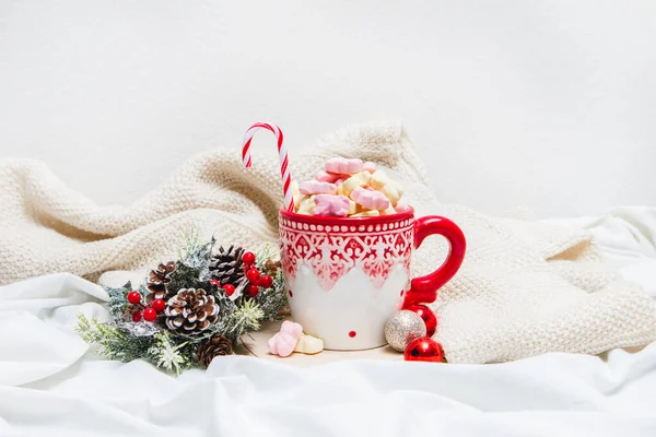 Red mug with marshmallows and winter ornaments on a white sheets