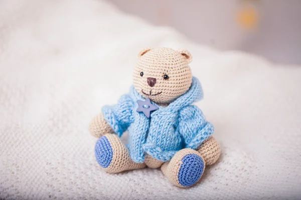 Orso all'uncinetto beige vestito su maglione blu su sfondo chiaro — Foto Stock