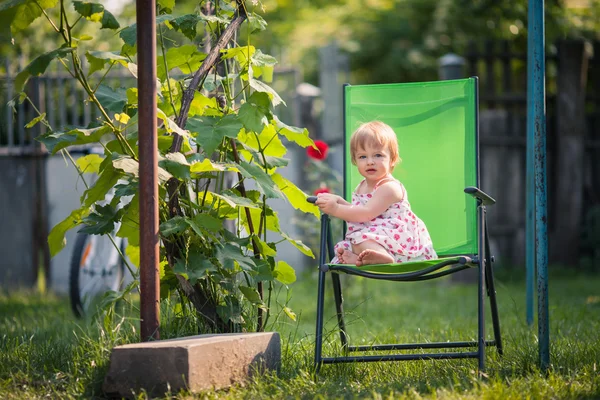 Bambina si siede sulla sedia da giardino vicino alla vite — Foto Stock