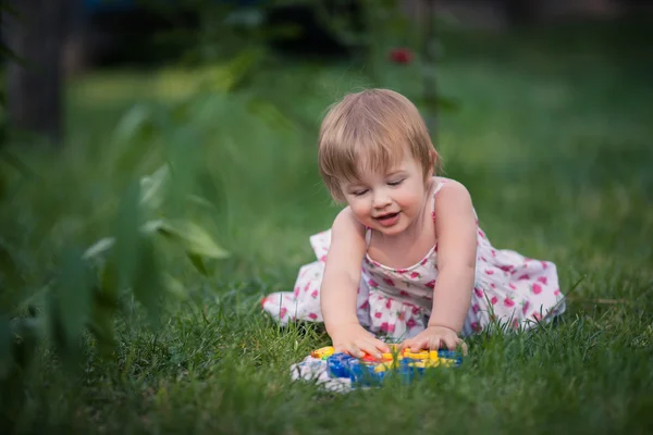 Bambina con gli occhi azzurri e capelli biondi gioca giocattolo sull'erba — Foto Stock