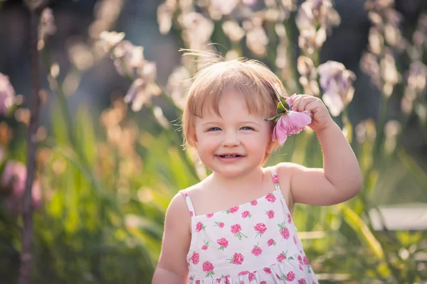 Baby girl in summer garden with bright flowers — Stock Photo, Image