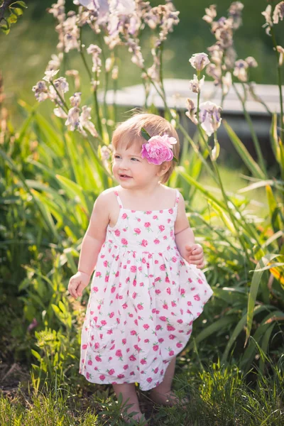 Baby flicka i sommar trädgård med ljusa blommor Royaltyfria Stockbilder