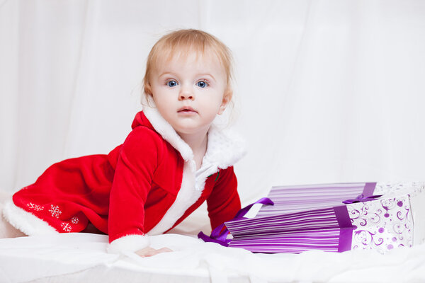 A little baby-girl dressed red fancy Santa Claus dress with violet paper-bag for gifts