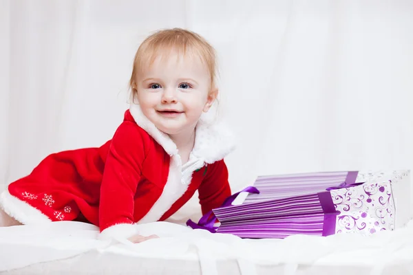 En liten flicka klädd röd fancy jultomten klänning med violett papperspåse för gåvor — Stockfoto