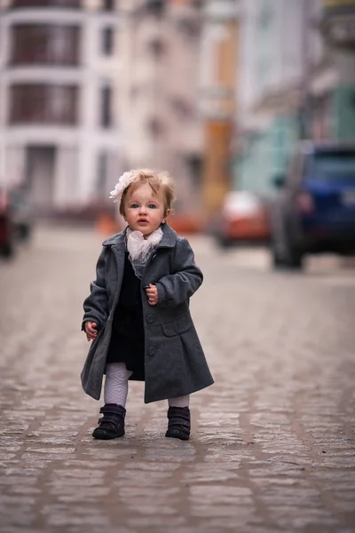 Una pequeña dama de abrigo gris y una gran flor en su oído se para en la calle — Foto de Stock
