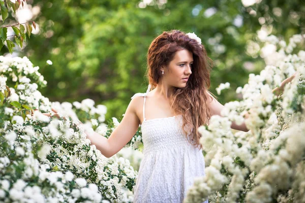 Encantadora joven con una hermosa sonrisa en el jardín de primavera lleno de flores blancas —  Fotos de Stock