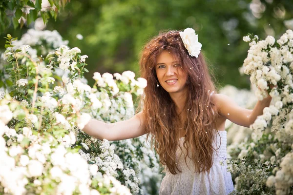 Hermosa joven con una sonrisa encantadora en el jardín de primavera lleno de flores blancas —  Fotos de Stock