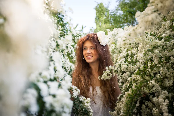 Retrato de una encantadora joven con una hermosa sonrisa en el jardín de primavera lleno de flores blancas —  Fotos de Stock