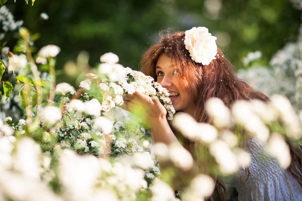 Charmig ung dam med vackert leende luktar gren av blommor i vår trädgård full av vita blommor — Stockfoto