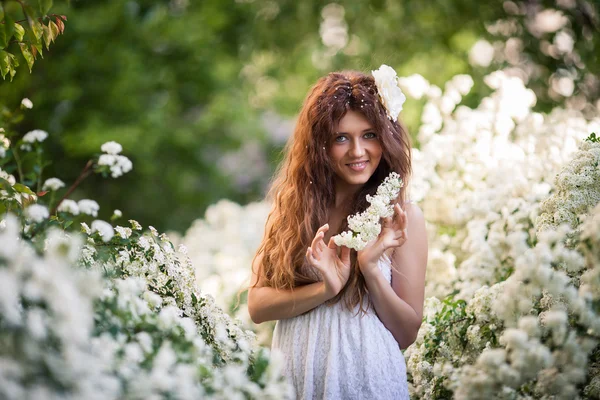 Jovem encantadora com belo sorriso mantém ramo florido no jardim da primavera cheio de flores brancas — Fotografia de Stock