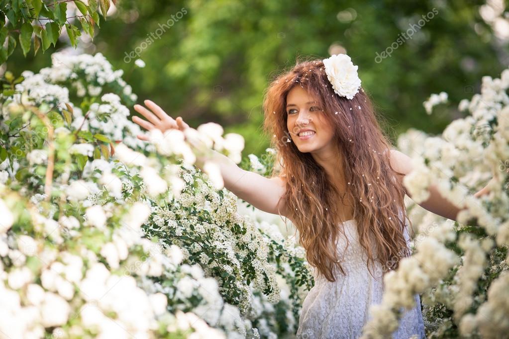 Beautiful young lady with charming smile in spring garden full of white flowers