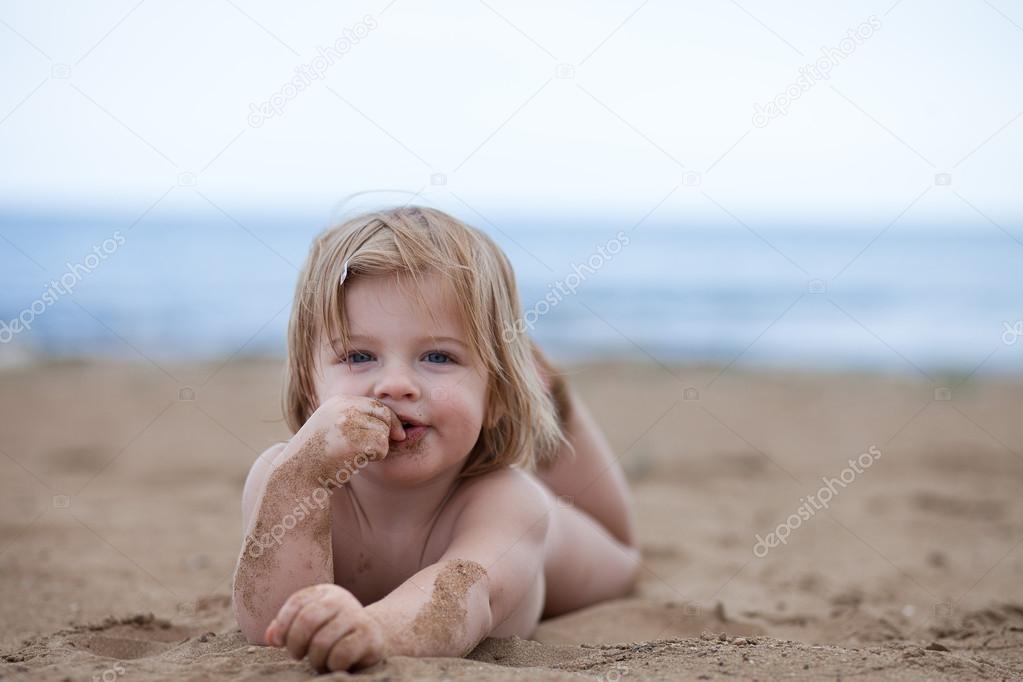 Little baby girl lie in the sun on the beach near the sea
