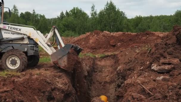 Escavadeira derrama sujeira em trincheira com tubo amarelo no local — Vídeo de Stock