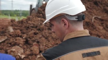 Beyaz kasklı işçi siper yakınında meslektaşıyla konuşuyor.