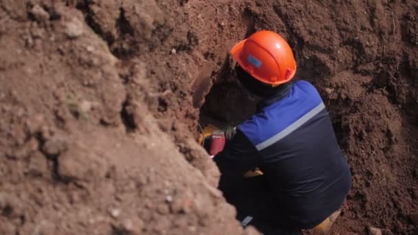 Laborer brousí žluté trubky plášť sedí uvnitř zákopu — Stock video